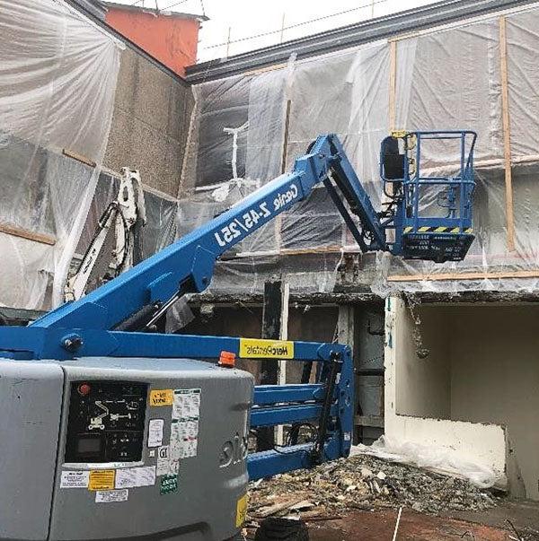 a lift truck in front of a 2-story building that is covered in plastic film